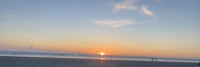 the sun is setting over a beach with people on it